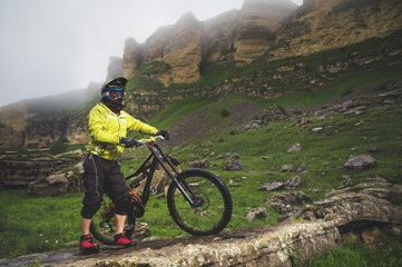 Side view of a man on a mountain bike standing on a rocky terrain and looking at a rock. The concept of a mountain bike and mtb downhill