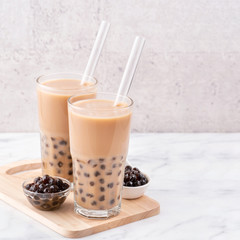 Tapioca pearl ball bubble milk tea, popular Taiwan drink, in drinking glass with straw on marble white table and wooden tray, close up, copy space.