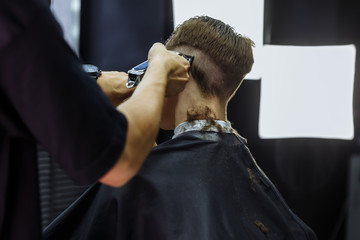Male haircut with electric razor. Barber makes haircut for client at the barber shop by using...