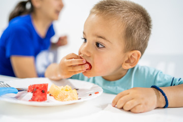 Little boy eating watermelon by the table at home