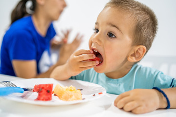 Little boy eating watermelon by the table at home