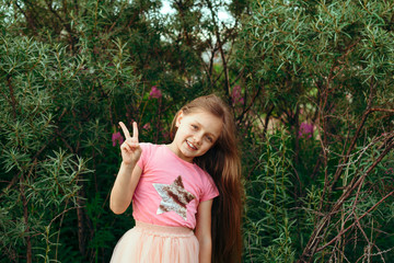 Portrait of a happy cheerful little  girl in summer park  showing peace gesture