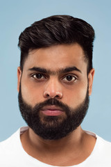 Obraz premium Close up portrait of young hindoo man with beard in white shirt isolated on blue background. Human emotions, facial expression, ad concept. Negative space. Standing and looking calm.