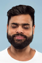 Fototapeta premium Close up portrait of young hindoo man with beard in white shirt isolated on blue background. Human emotions, facial expression, ad concept. Negative space. Dreaming with eyes closed.