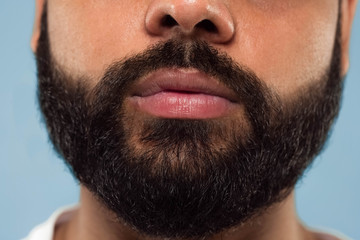 Obraz premium Close up portrait of young hindoo man's face with beard and lips on blue background. Looking calm. Human emotions, facial expression, advertising concept. Negative space.
