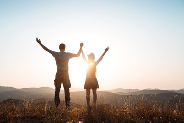 Fototapeta na wymiar The guy and girl stands among the mountains and greet the sun