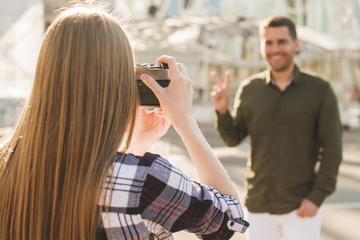 Rear view of blonde hair woman taking picture of man with peace gesture