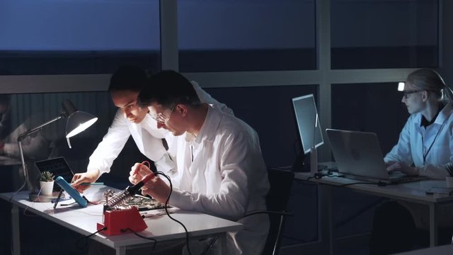 Multiracial man and woman checking motherboard with multimeter tester in electronics laboratory. They discussing and explaining different things