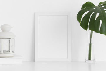 White frame mockup with workspace accessories and a monstera leaf in a vase on a white table.Portrait orientation.