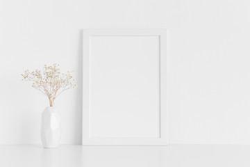 White frame mockup with a gypsophila in a vase on a white table.Portrait orientation.