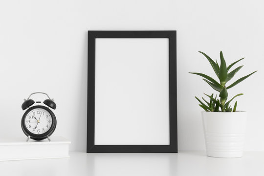 Black frame mockup with workspace accessories and a aloe vera on a white table.Portrait orientation.