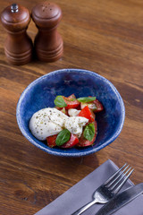 Salad with Italian white burrata cheese served with tomatoes and pesto on blue plate on wooden background. Healthy, tasty, food. Diet, holidays, recipe concept. Free space for text. Selective focus