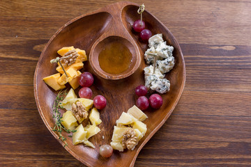 Top view of tasty cheese plate with grape, nuts and honey on wooden plate. Copy space. Gourmet food. Diet, holidays, healthy concept. Selective focus