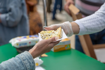 The seller gives the buyer a slice of pizza on the street. Street food. Close up.