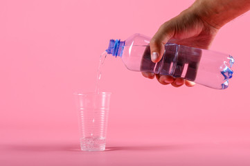 Male Pouring water from bottle into plastic cup on pink background