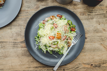 Healthy Grilled Chicken Caesar Salad with Cheese and Croutons on black plate. Top view