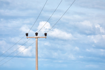Concrete high voltage power electric pole with power lines and fuses against sky background.
