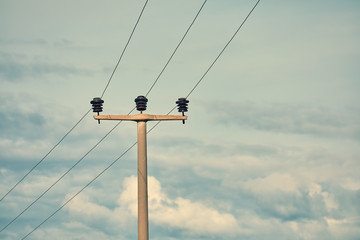 Concrete high voltage power electric pole with power lines and fuses against sky background.