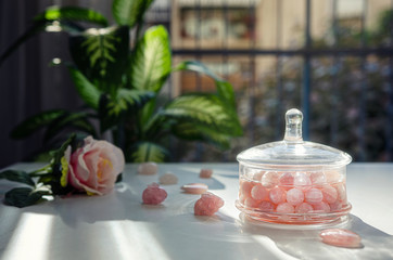Rose quartz beads are filled up spring water in a glass jar. Making homemade gem elixir with  semiprecious stones on the balcony table.