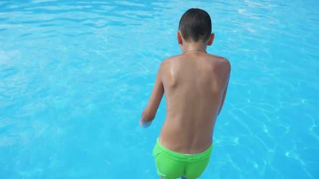 Small boy in yellow shorts jumping feet first in a swimming pool in slow motion