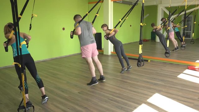 The trainer teaches in the gym to practice a man on the hinges of the TRX while performing an exercise facial thrust, group lesson, workout