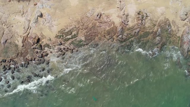 Aerial view of tropical rock on beach which the waves draw back, and fling footage,  beuatiful blue ocean and rock coastal and waves crashing in tranquil bay.
