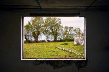 Interior of a ruined house with a broken window frame viewing a green meadow field landscape