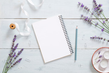 Empty paper notepad, pen, lavender flower, ribbon on rustic blue wooden desk. Flat lay, top view, overhead. Fashion blogger workspace, feminine office desk.
