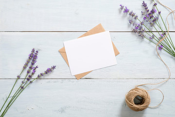 Vintage envelope, blank paper card, lavender flowers and twine on rustic blue wooden background. Romantic composition, love love letter concept. Flat lay, top view, overhead.