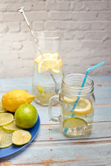 view of a jug of lemonade with ice and lemon next to a blue plate with limes and lemon