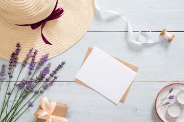 Flatlay composition with straw hat, lavender flowers, paper card mockup, craft envelope, ribbon,...