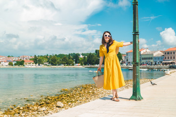 woman walking by sea quay in summer day in yellow sundress