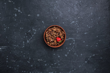 Obraz na płótnie Canvas Granola with a ripe strawberry in a ceramic bowl on a dark stone surface. Top view.