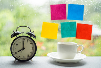 Fototapeta na wymiar Vintage clock time at eight o'clock and coffee cup with blur post it stick on windows in raining day