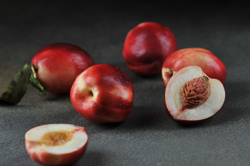 Fototapeta na wymiar Ripe nectarines on the table. One of the nectarines is cut in half. Close-up. Dark background.