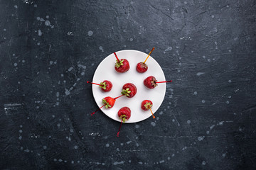 Strawberry berries on chopsticks for snacks in a white plate on a dark stone surface. Top view.