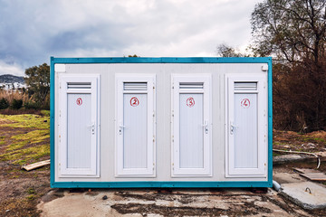 Prefabricated portable cabin with four doors with numbers on them on a meadow field in the forest