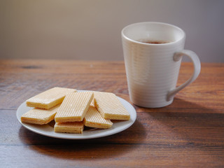 Waffles on a white plate and a cup of hot tea on a wooden table. Breakfast concept.