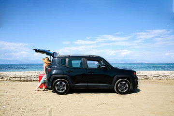 Fototapeta na wymiar A woman in a hat and sunglasses and a car on a sunny sandy beach