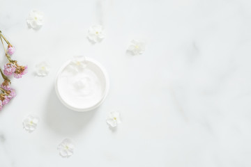 Obraz na płótnie Canvas White moisturizing cream with flower petals on marble background. Skin care beauty treatment with jar of body moisturizer. Bio organic, natural beauty products concept.