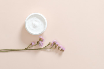 Jar with moisturizing body cream and dry flower on pastel pink background. Skin care cosmetic, anti aging concept. Minimal flat lay style composition, top view, copy space.