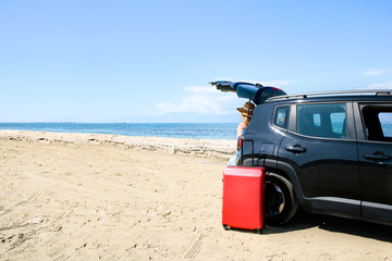 A woman in a black car on a sandy beach and blue ocean view.