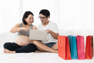 Fototapeta premium husband and chubby wife who is pregnant shopping online use baby on laptop wifi internet in the white bedroom