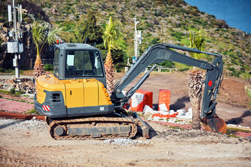 Yellow excavator performing excavation work in a construction site near the seaside. Its bucket is stucked in soil.