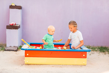 Cute baby boy playing with his sister in the sandbox