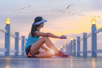 woman sport runner sitting on the wooden sea bridge holding drinking water in hand, resting or...
