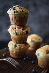 Crumble top blueberry muffins in pile on oak board on dark background with natural lighting