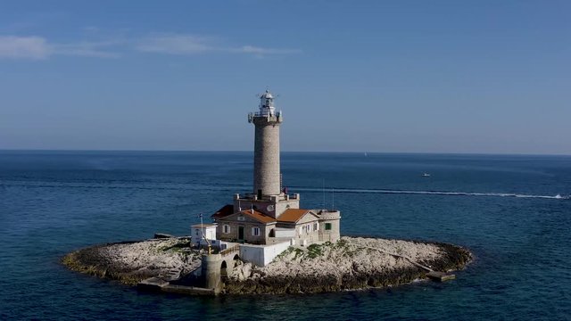 AERIAL circling shot of a lighthouse on a tiny island off the coast of Croatia