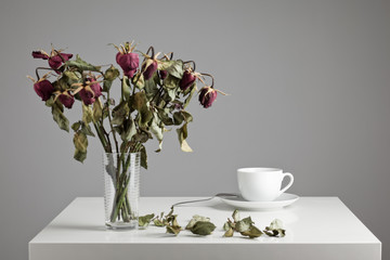 Cup of coffee with dried, dead flowers on a table