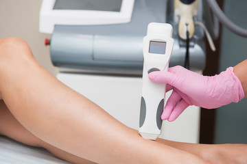 Specialist makes skin tone measurements on a womans leg, to determine the settings for hair laser depilation. First step before depilation. Cosmetology and SPA concept